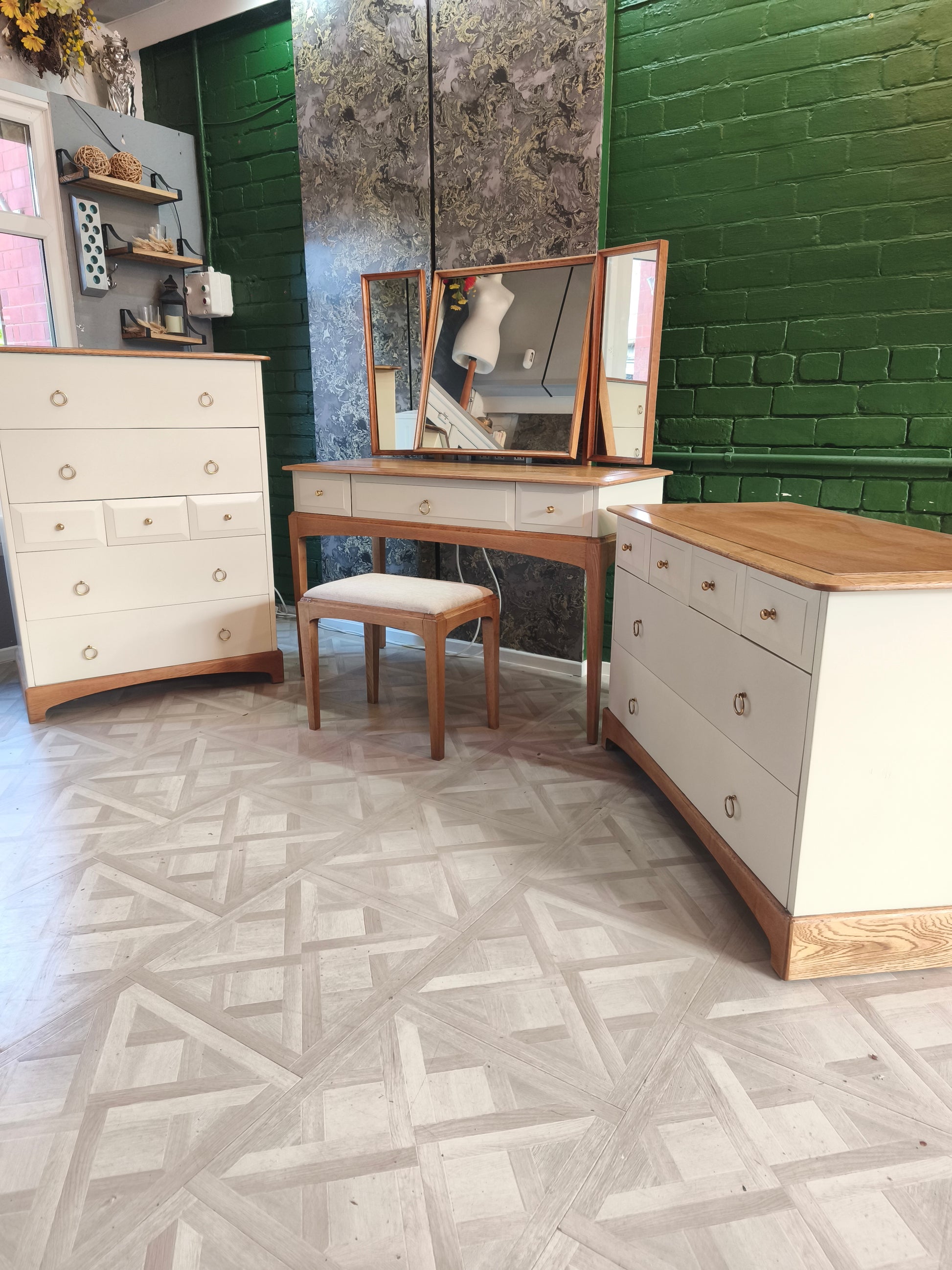 Wooden furniture including a dresser, vanity table, and chair in a room with green brick walls.